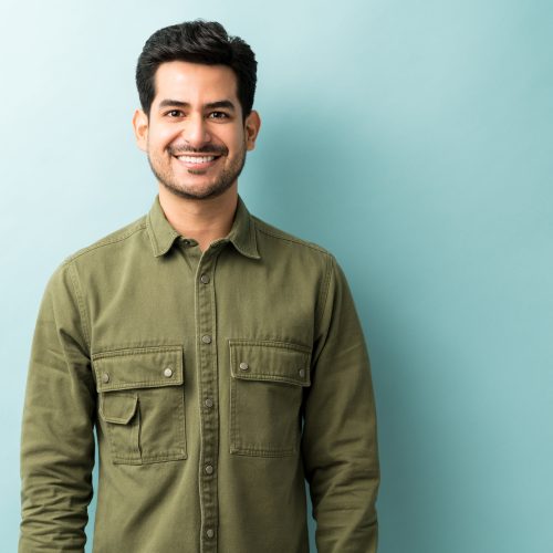 handsome-smiling-man-wearing-green-shirt-standing-against-blue-background-min